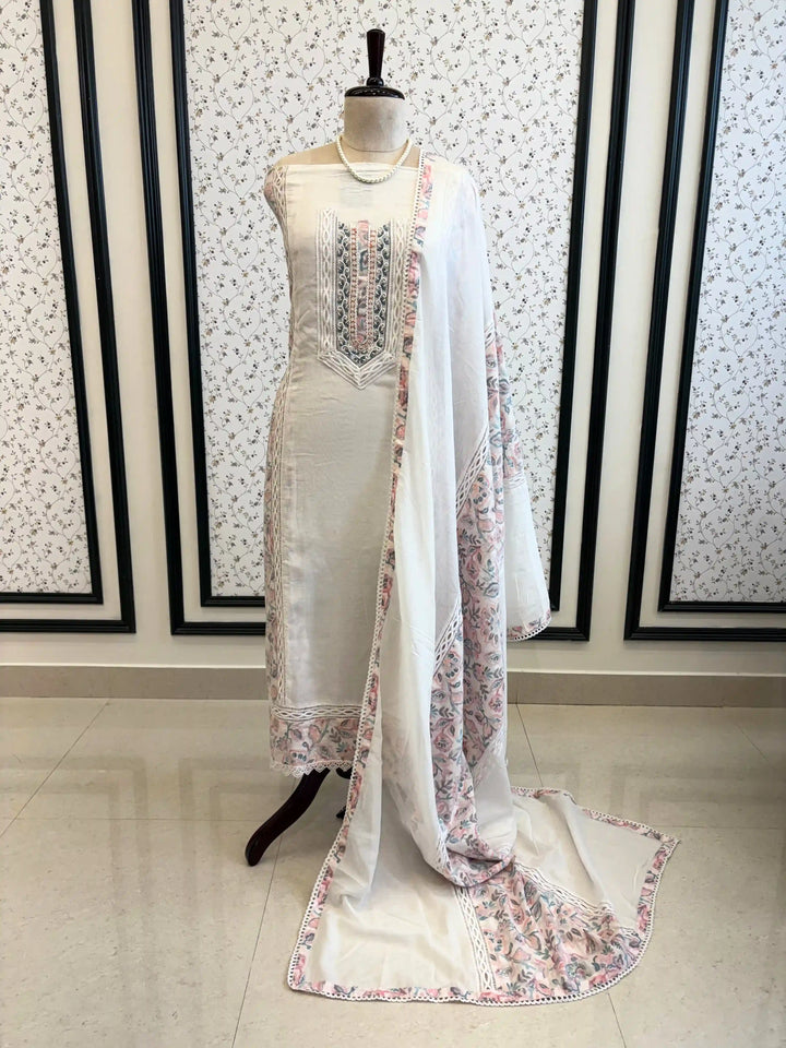 White cotton unstitched suit with embroidered neckline, lace detailing, and pastel floral organza dupatta for summer festive wear.