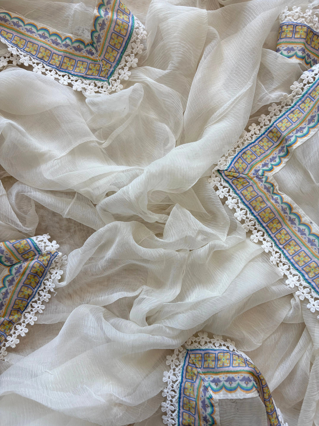 White cotton unstitched suit with embroidered neckline, lace detailing, and chiffon dupatta for summer festive wear.