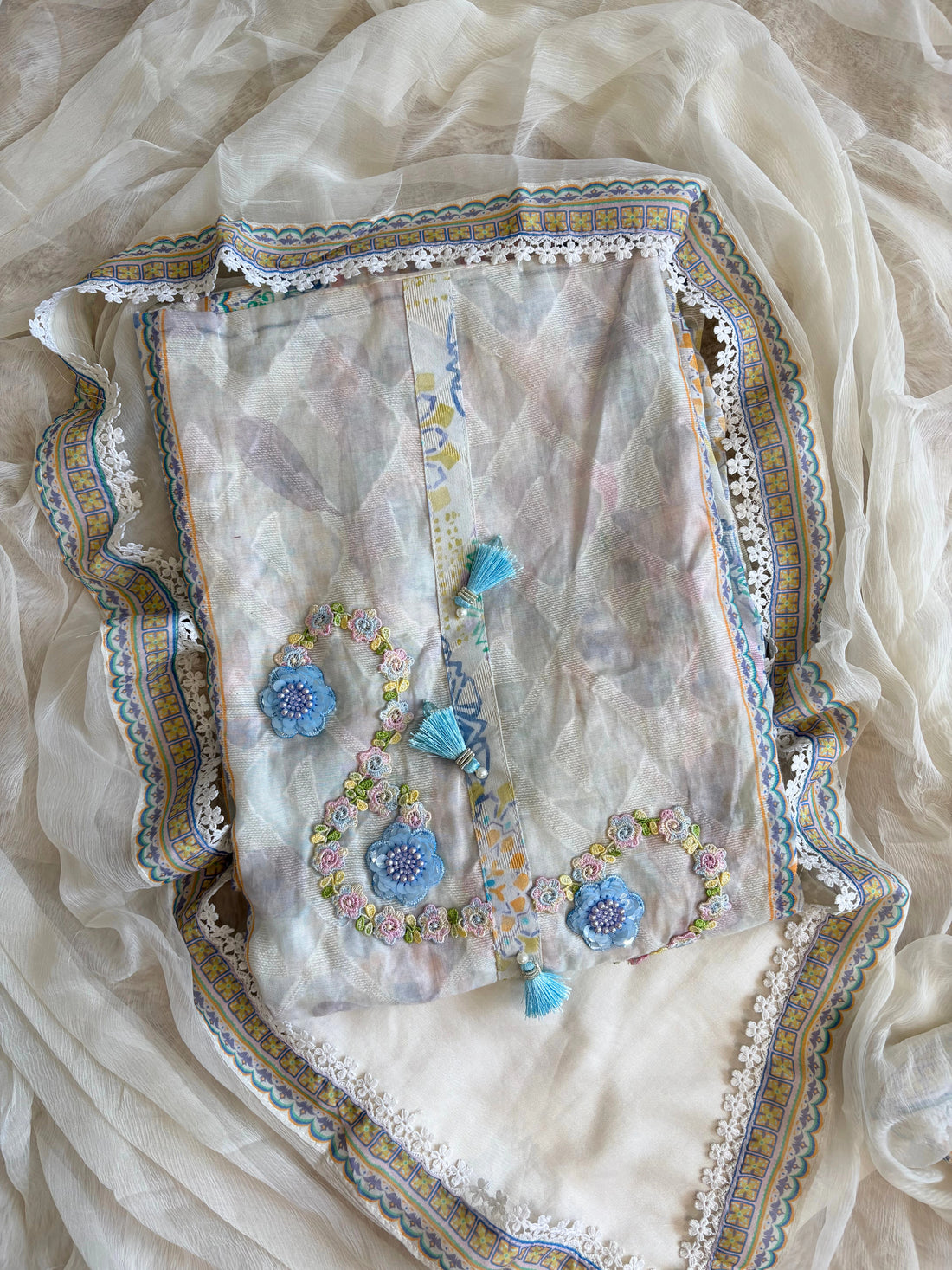 White cotton unstitched suit with embroidered neckline, lace detailing, and chiffon dupatta for summer festive wear.