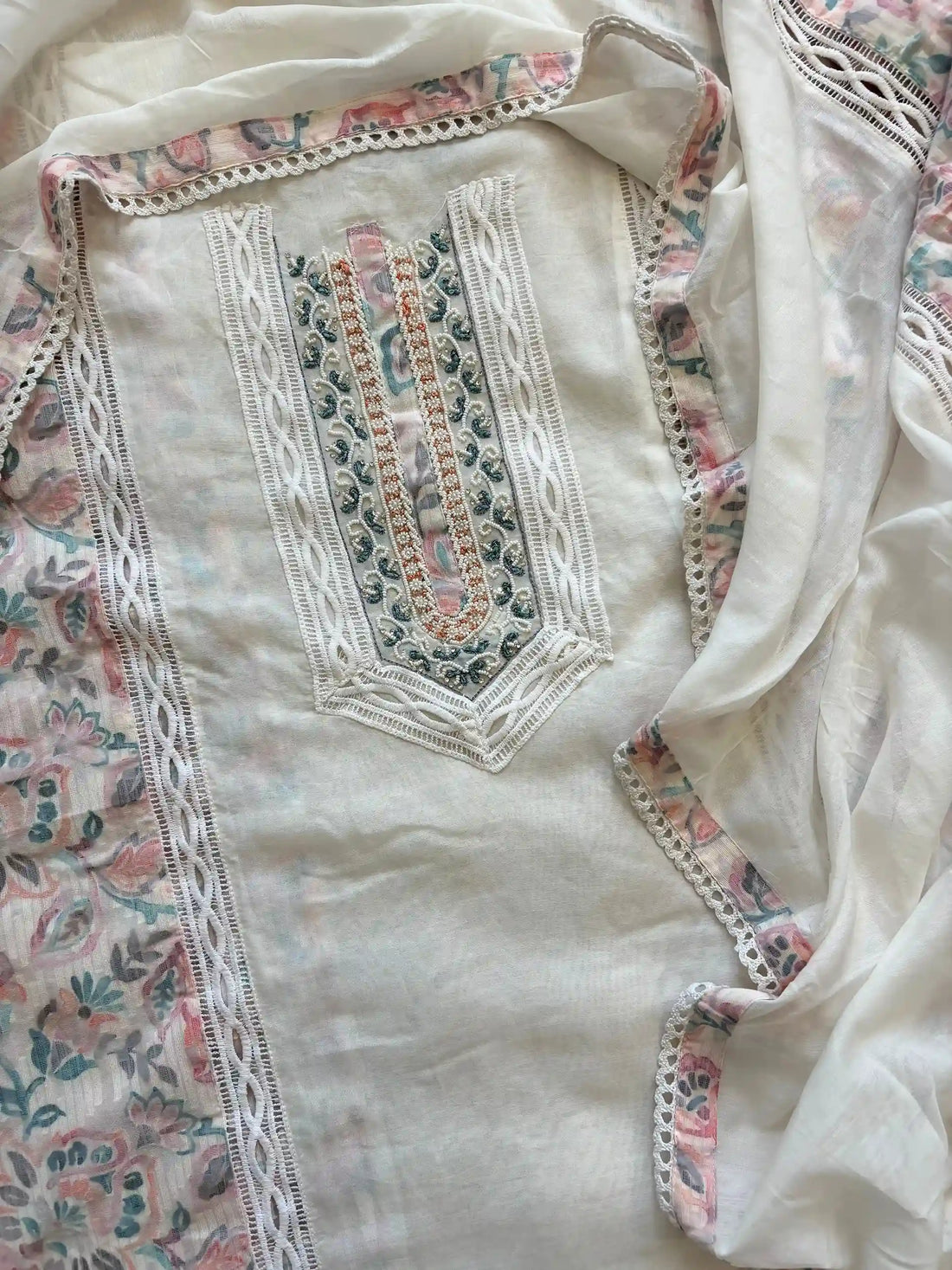 White cotton unstitched suit with embroidered neckline, lace detailing, and pastel floral organza dupatta for summer festive wear.