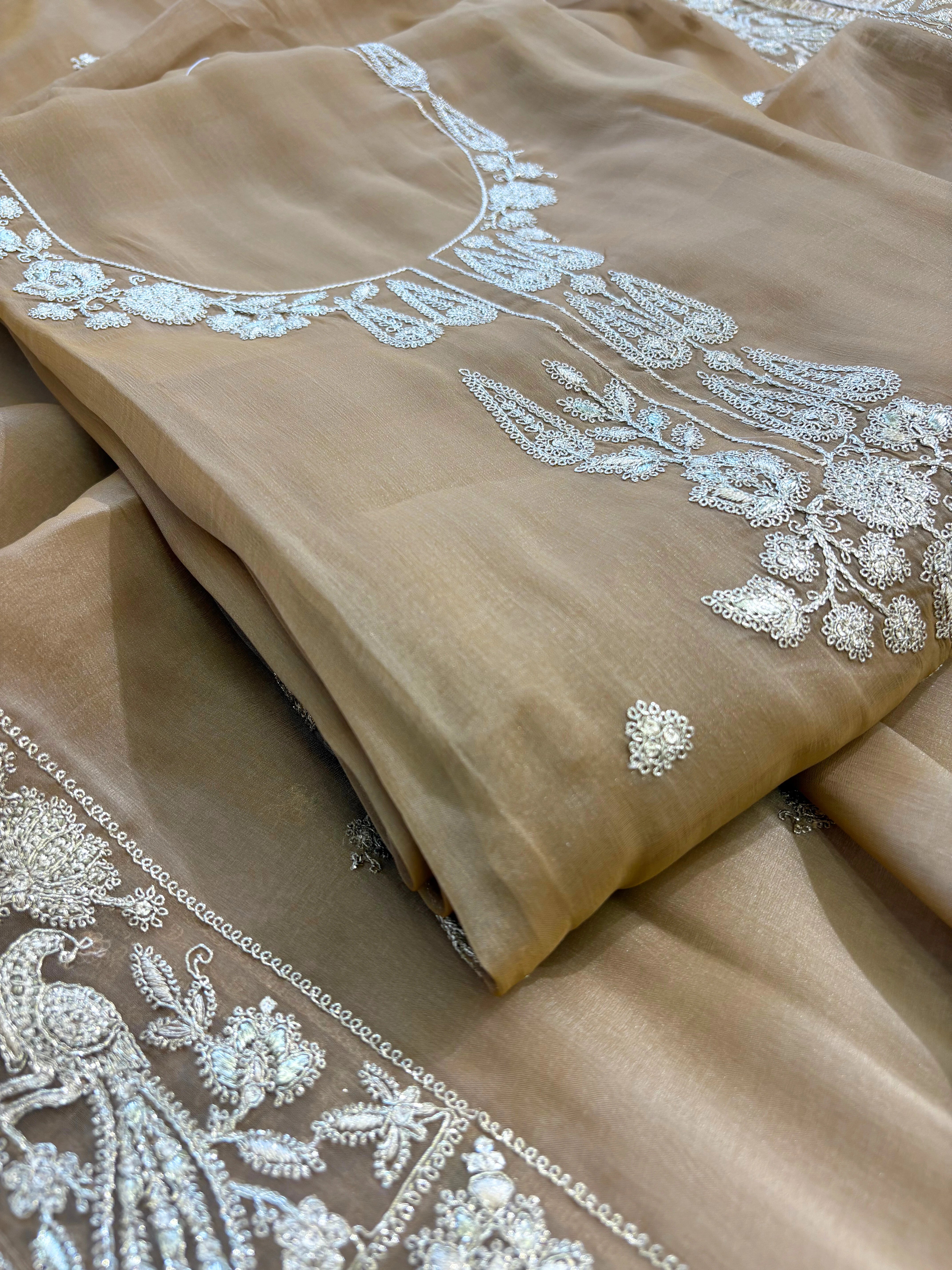 Beige organza unstitched suit with golden zari embroidery and embroidered dupatta, ideal for weddings and festive celebrations.