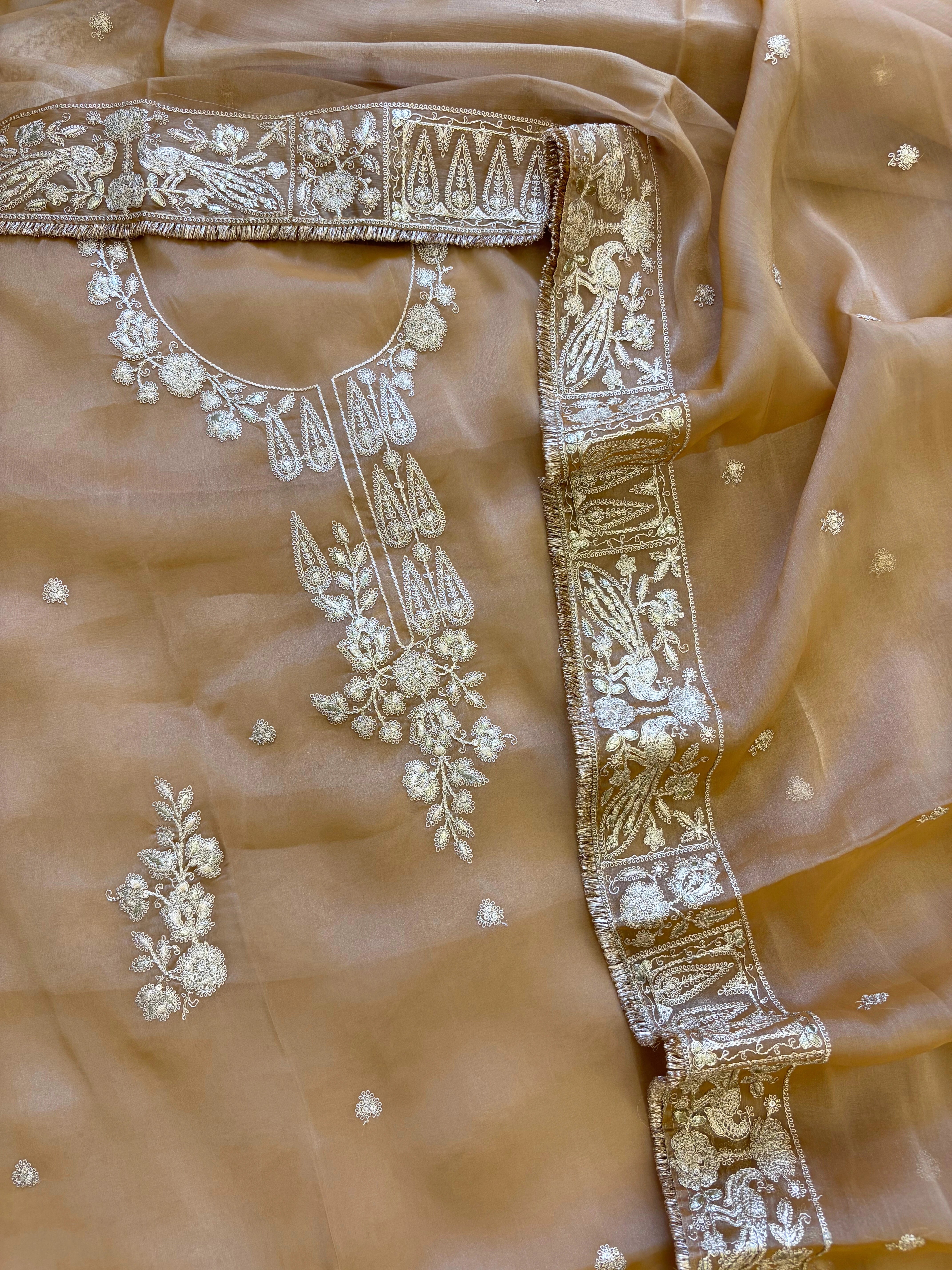 Beige organza unstitched suit with golden zari embroidery and embroidered dupatta, ideal for weddings and festive celebrations.