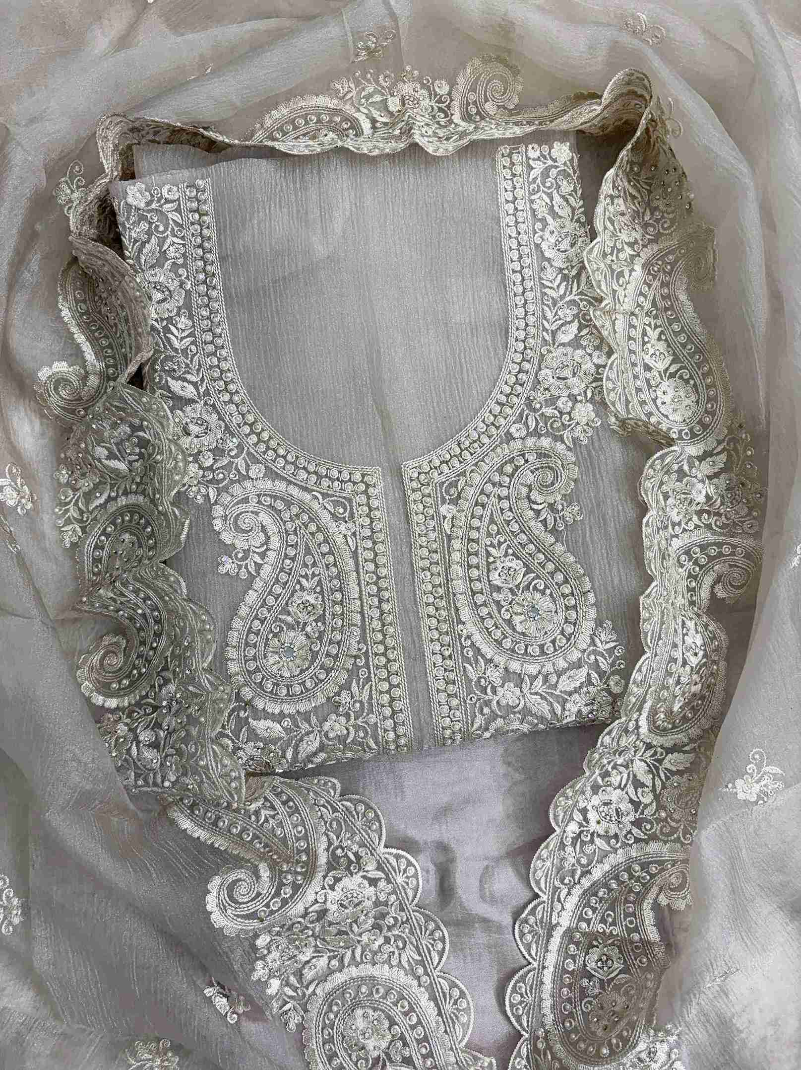 Close-up of intricate paisley neckline with cutdana, sequins, and pearl embellishments on beige marble chiffon shirt
