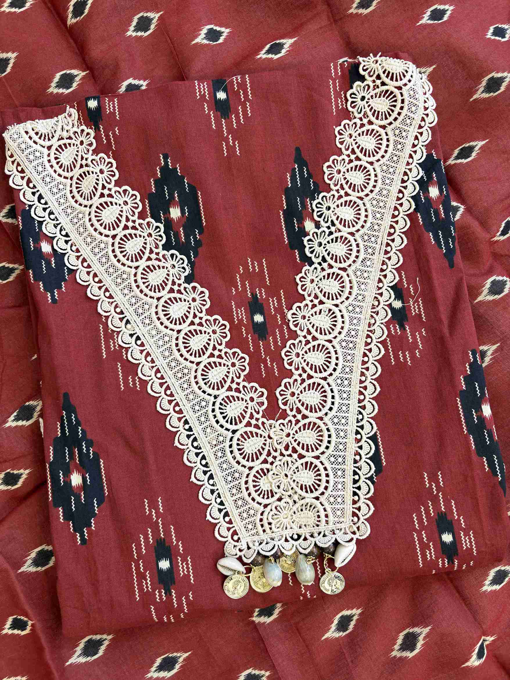 V-shaped neckline with broad cream crotia lace highlighting and decorative tassels on brick red cotton shirt