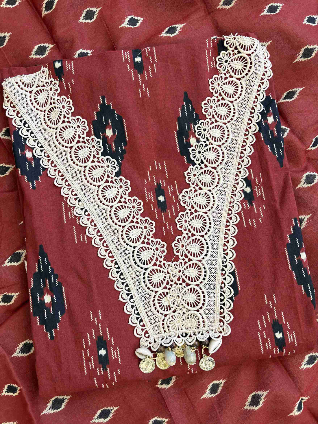V-shaped neckline with broad cream crotia lace highlighting and decorative tassels on brick red cotton shirt