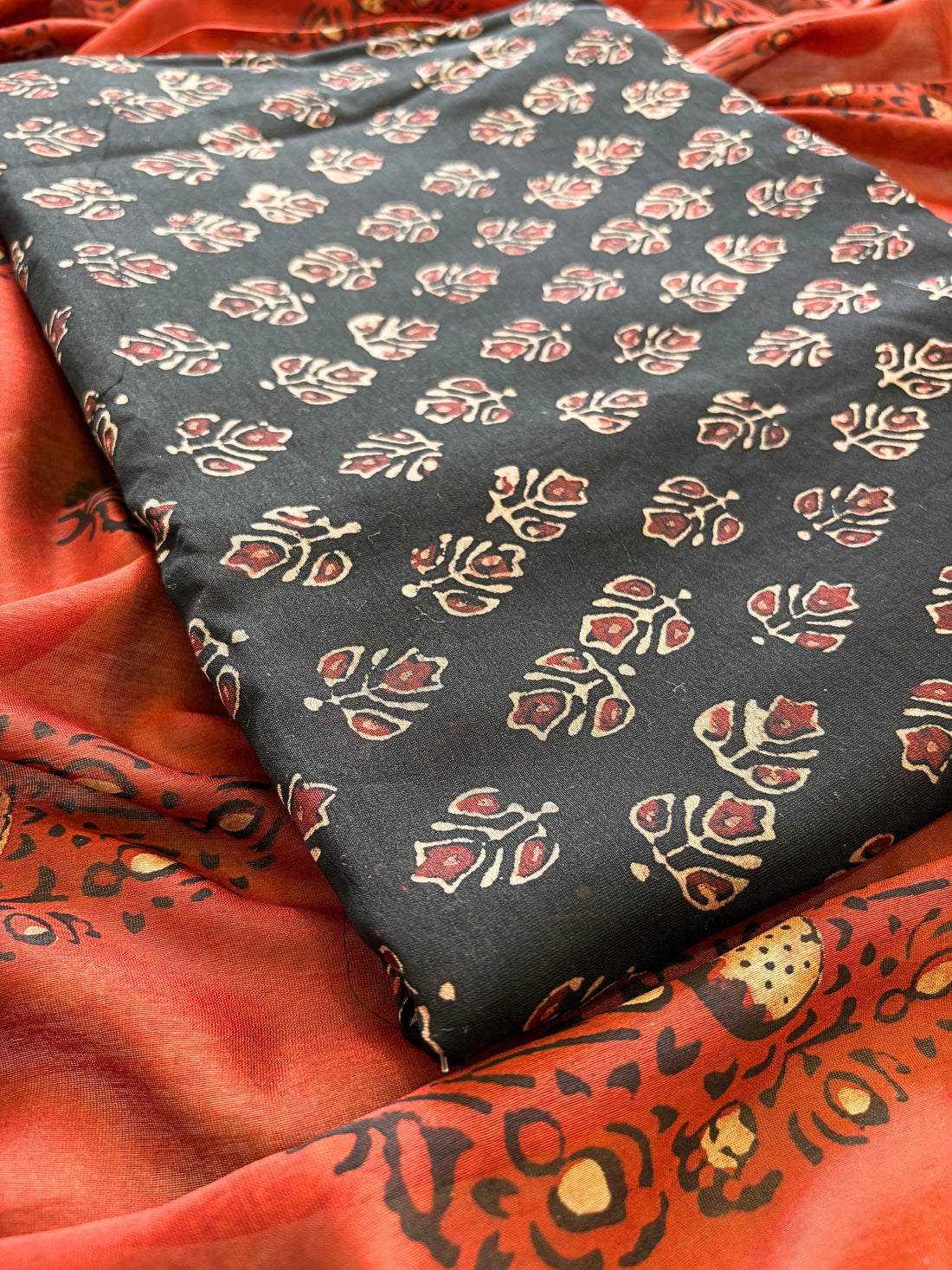 Black Maheshwari silk unstitched suit with hand block floral print, paired with rust dupatta featuring bold ethnic motifs – elegant festive ethnic wear