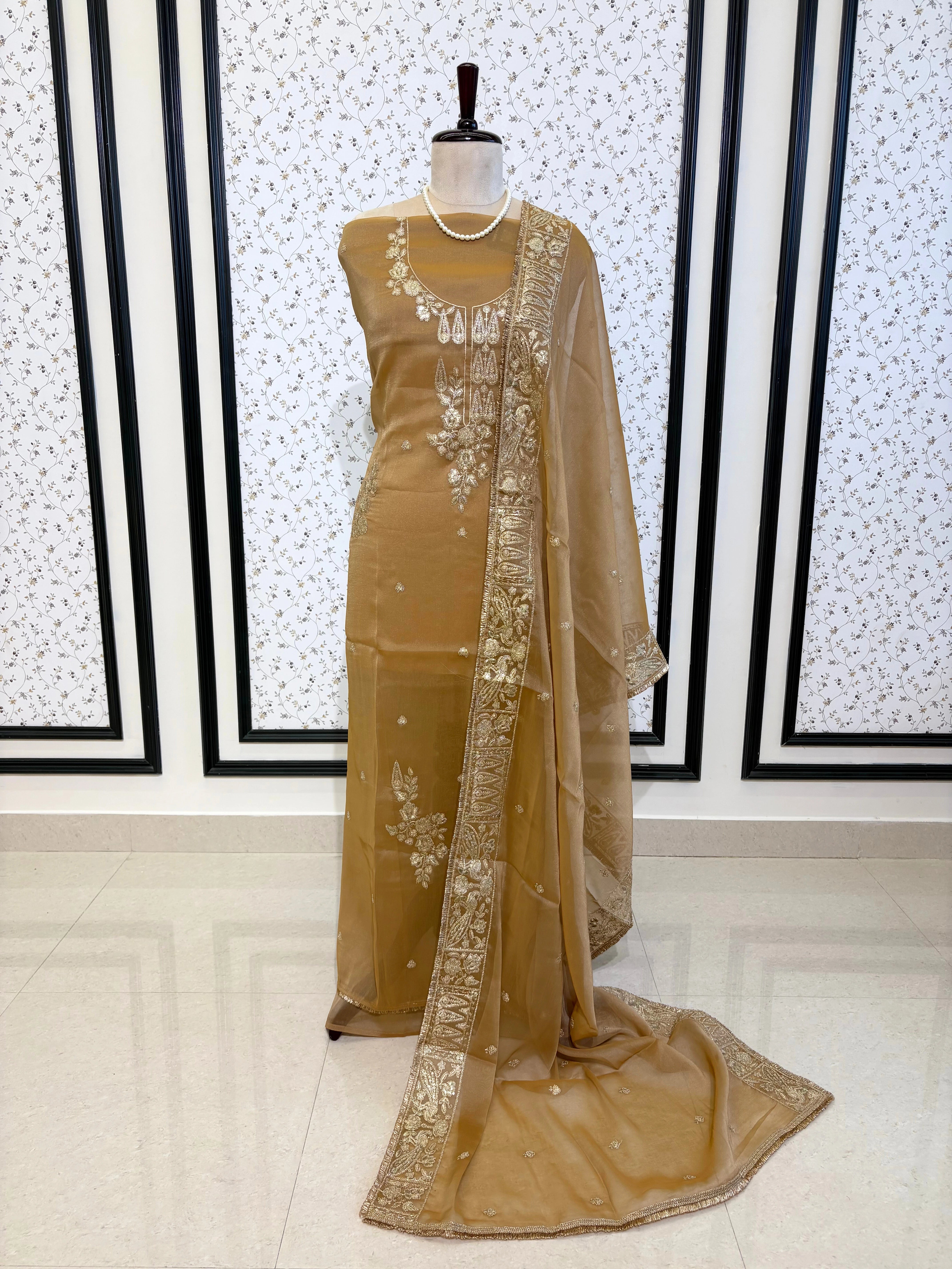 Beige organza unstitched suit with golden zari embroidery and embroidered dupatta, ideal for weddings and festive celebrations.