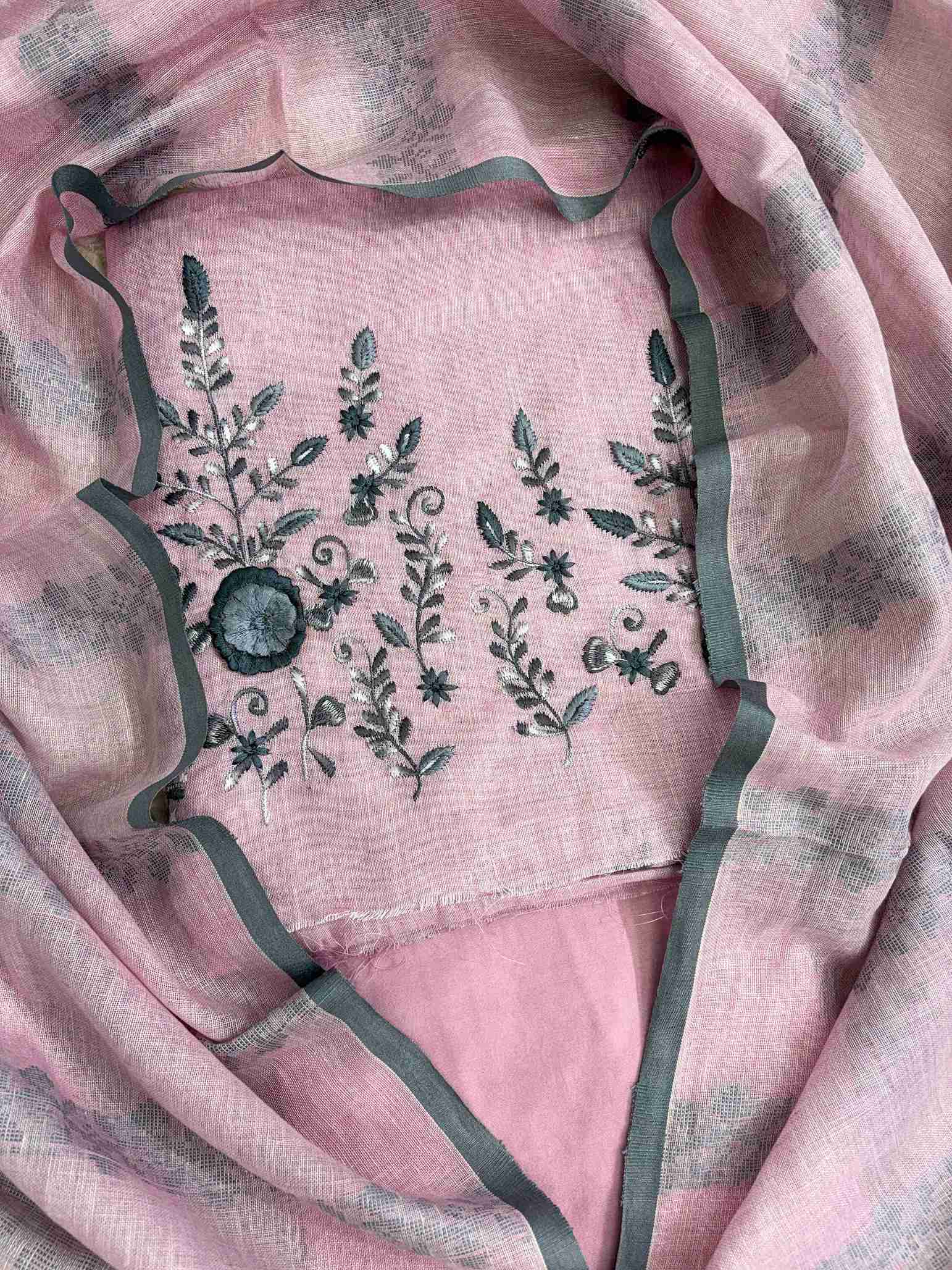 Close-up of contrasting thread embroidery with floral and botanical motifs on dusty pink linen shirt hemline