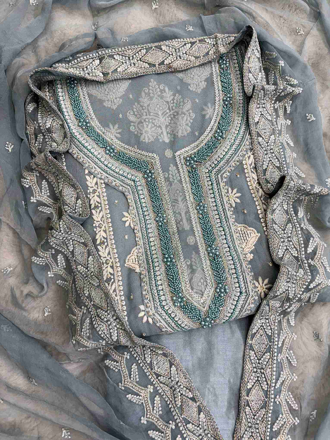 Front view of dusty teal georgette unstitched suit featuring intricate thread and sequin embroidery