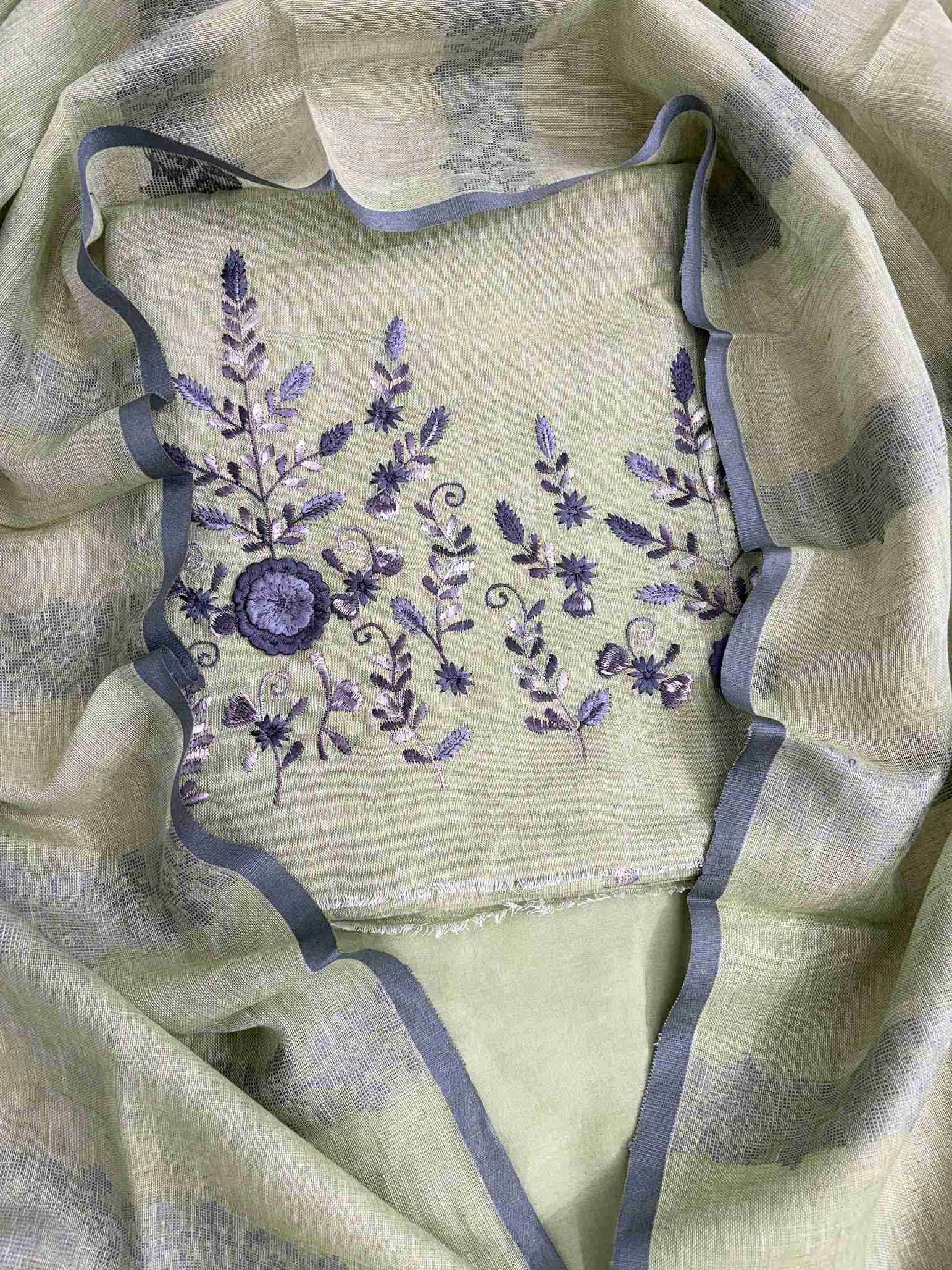 Close-up of contrasting thread embroidery with floral and botanical motifs on mint green linen shirt hemline