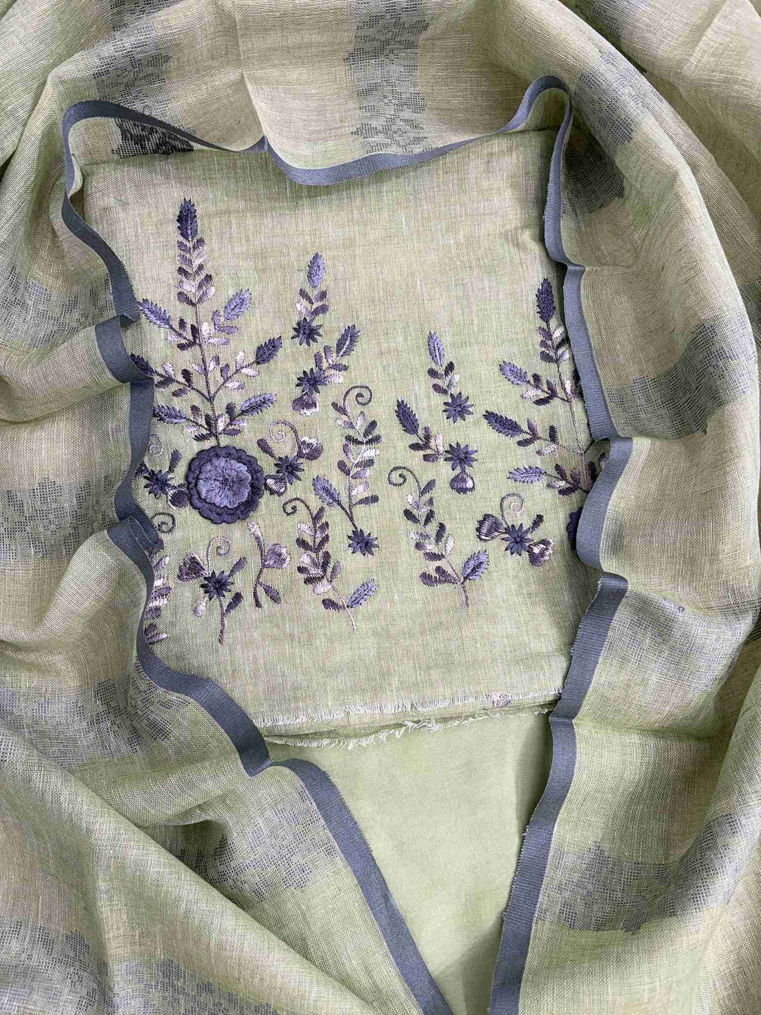Close-up of contrasting thread embroidery with floral and botanical motifs on mint green linen shirt hemline