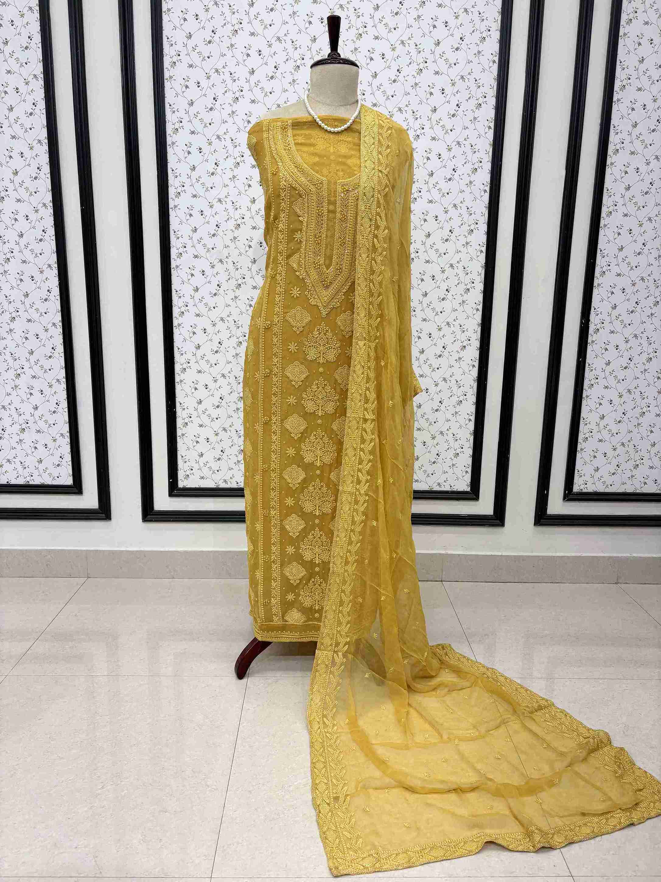 Mustard yellow embroidered unstitched suit displayed on mannequin with flowing chiffon dupatta