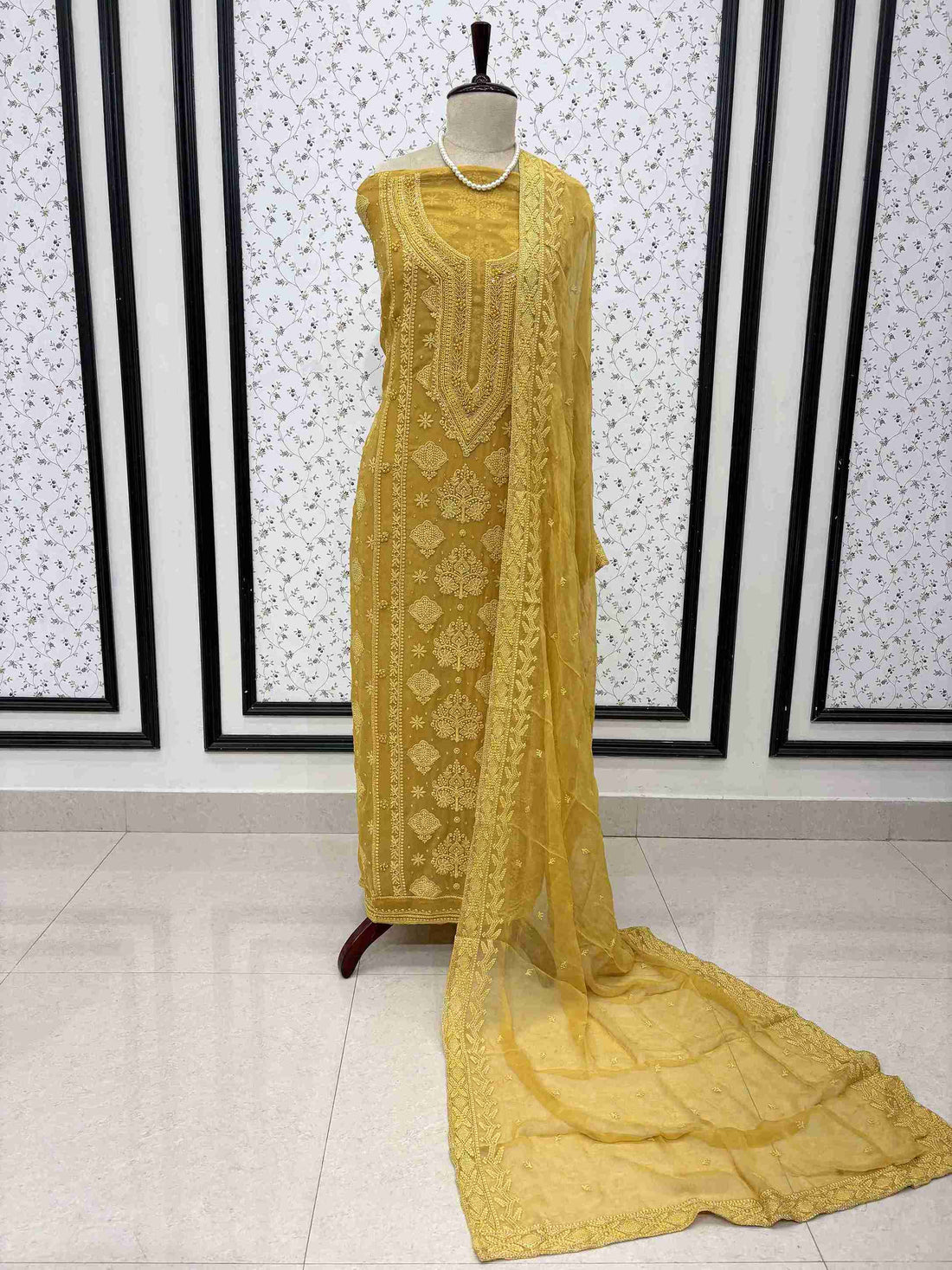 Mustard yellow embroidered unstitched suit displayed on mannequin with flowing chiffon dupatta