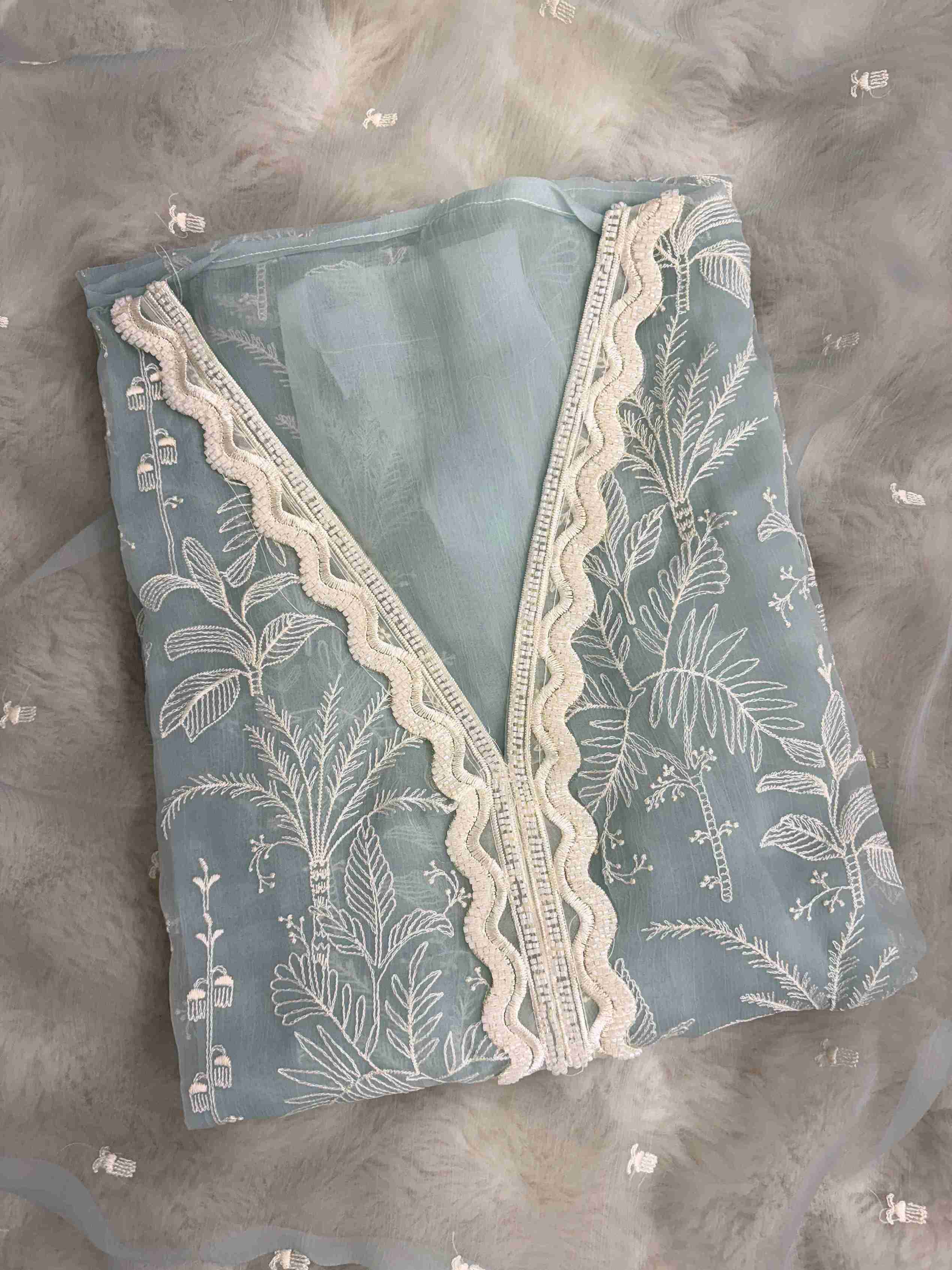 Close-up of V neckline with white cutwork lace and resham embroidery on powder blue suit