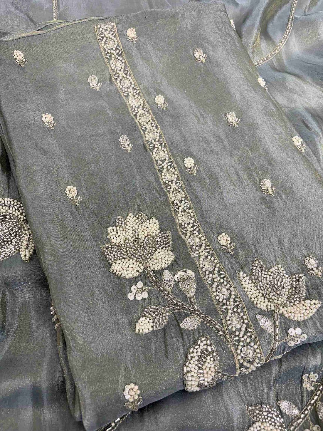 Close-up of richly embellished neckline with thread embroidery, pearls, nalki, beads, and sequins on sage grey-green soft tissue shirt