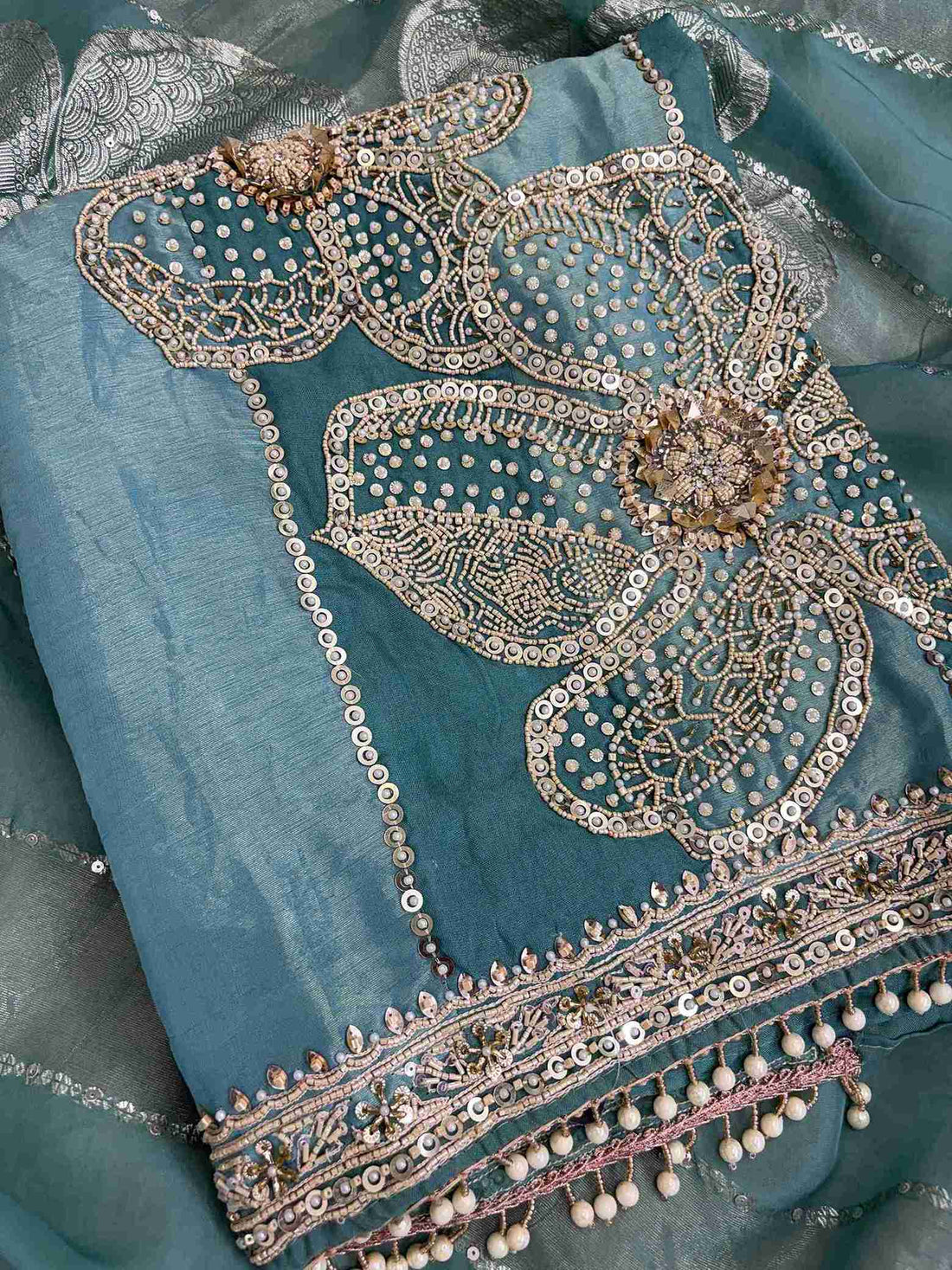 Close-up of teal organza shirt hemline featuring intricate cutdana handwork