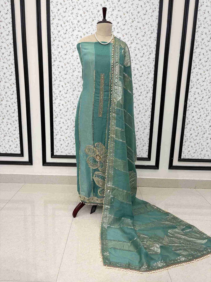 Teal shimmer organza unstitched suit set displayed on mannequin with cutdana hemline and Banarasi dupatta
