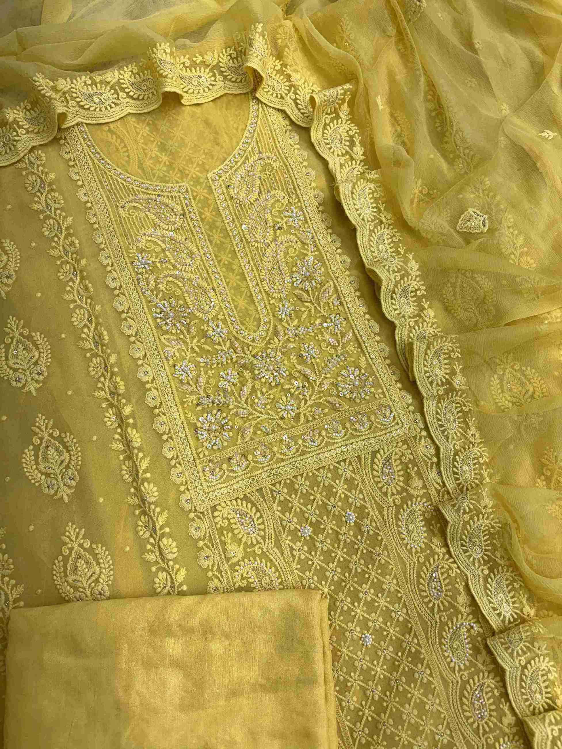 Complete yellow georgette unstitched suit flat lay set with chikankari shirt, chiffon dupatta, and cotton silk bottom