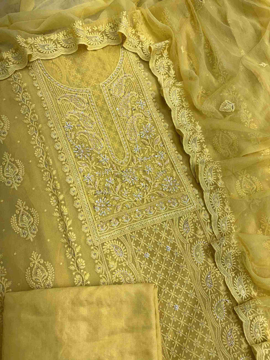 Complete yellow georgette unstitched suit flat lay set with chikankari shirt, chiffon dupatta, and cotton silk bottom