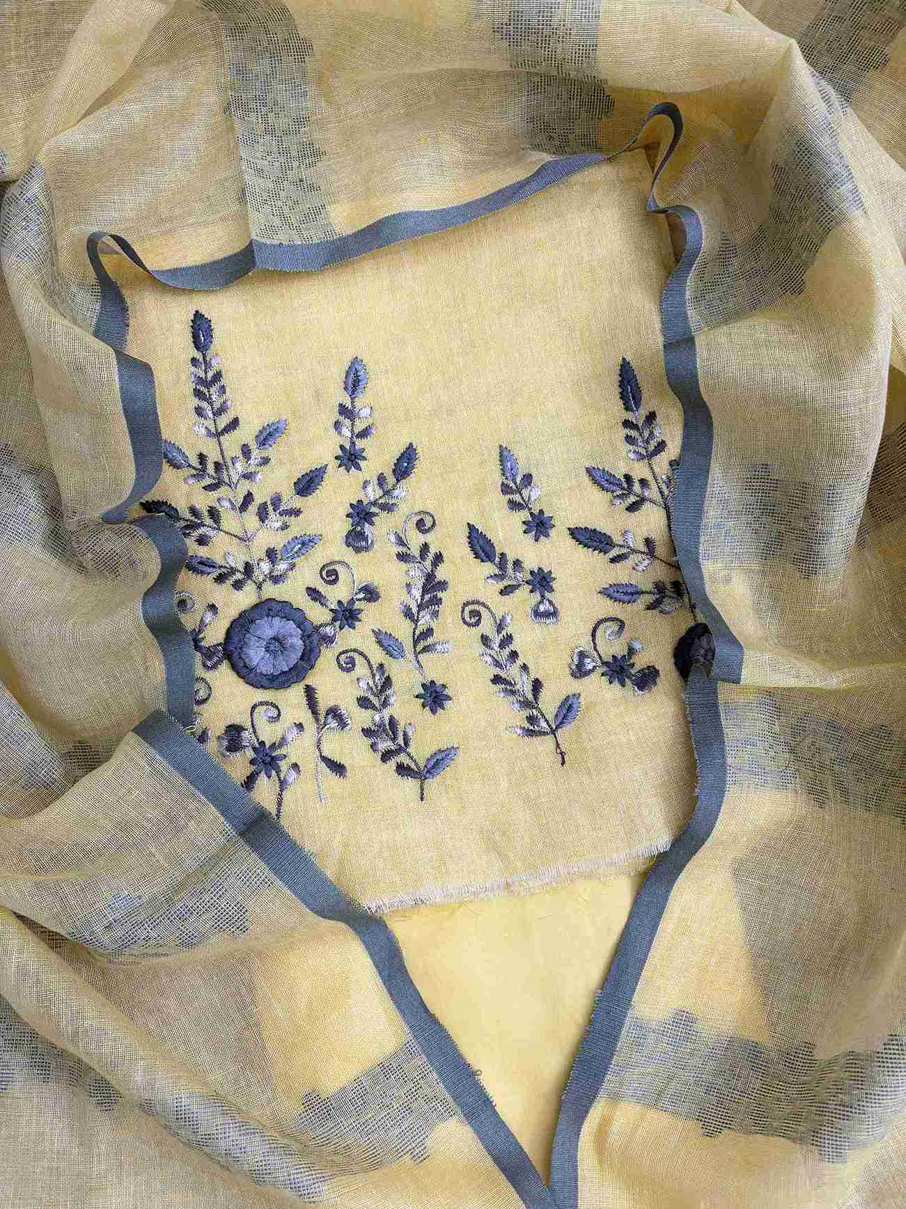 Close-up of contrasting thread embroidery with floral and botanical motifs on yellow linen shirt hemline